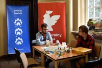 Dorośli i dzieci grający w gry planszowe przy bibliotecznych stolikach.