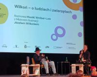 Mężczyzna i kobieta prowadzą rozmowę na scenie. W tle telebim