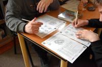 Zbliżenie na dłonie dwóch uczniów siedzących przy stole, którzy wypełniają karty pracy.