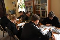 Grupa nastoletnich chłopców siedzi przy stolikach w bibliotece, wypełniają karty pracy.