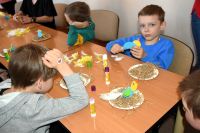 Grupa chłopców siedzi przy stolikach, wykonują ptaszki z papieru.