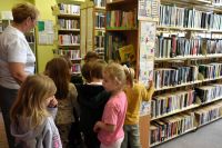 Grupa dzieci stoi w bibliotece przy regale z książkami.