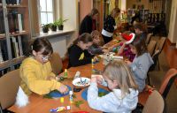 Dzieci wykonujące własnoręcznie ozdoby bożonarodzeniowe na świątecznych warsztatach w bibliotece.