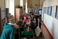 Uczestnicy spotkania Planszówki w bibliotece, dzieci i osoby dorosłe siedzą przy stolikach i grają w gry planszowe