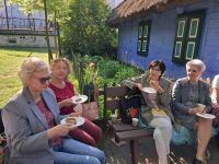 Uczestniczki spotkania DKK, siedzące na ławkach w skansenie.