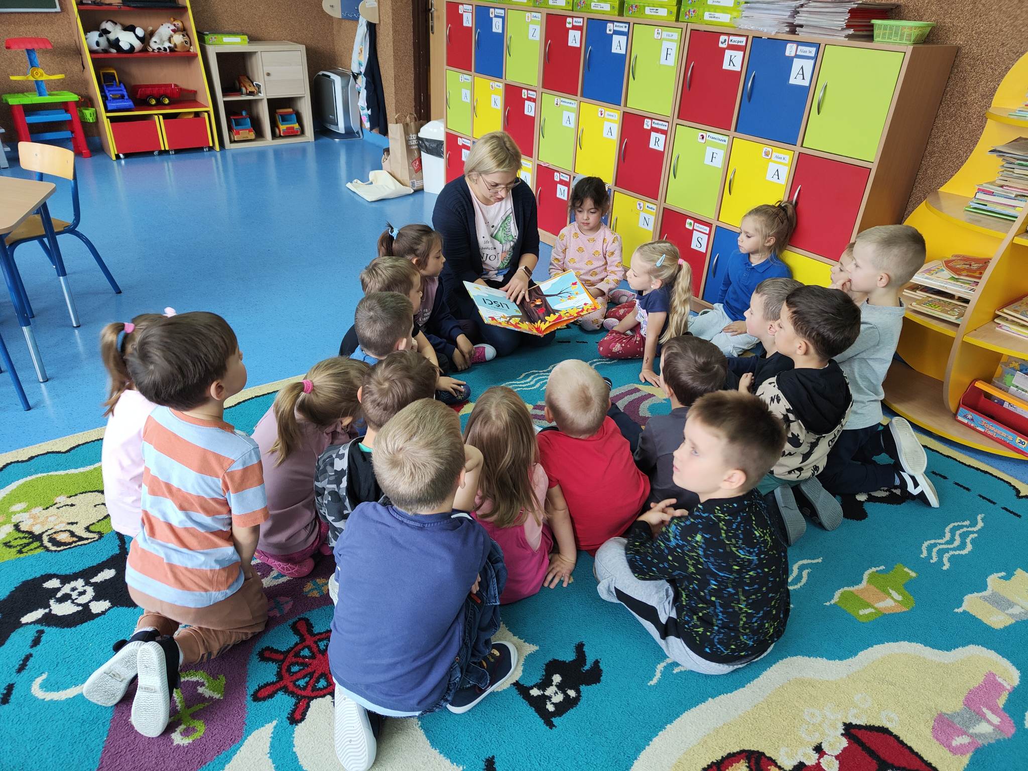 Dzieci siedzą na kolorowym dywanie.