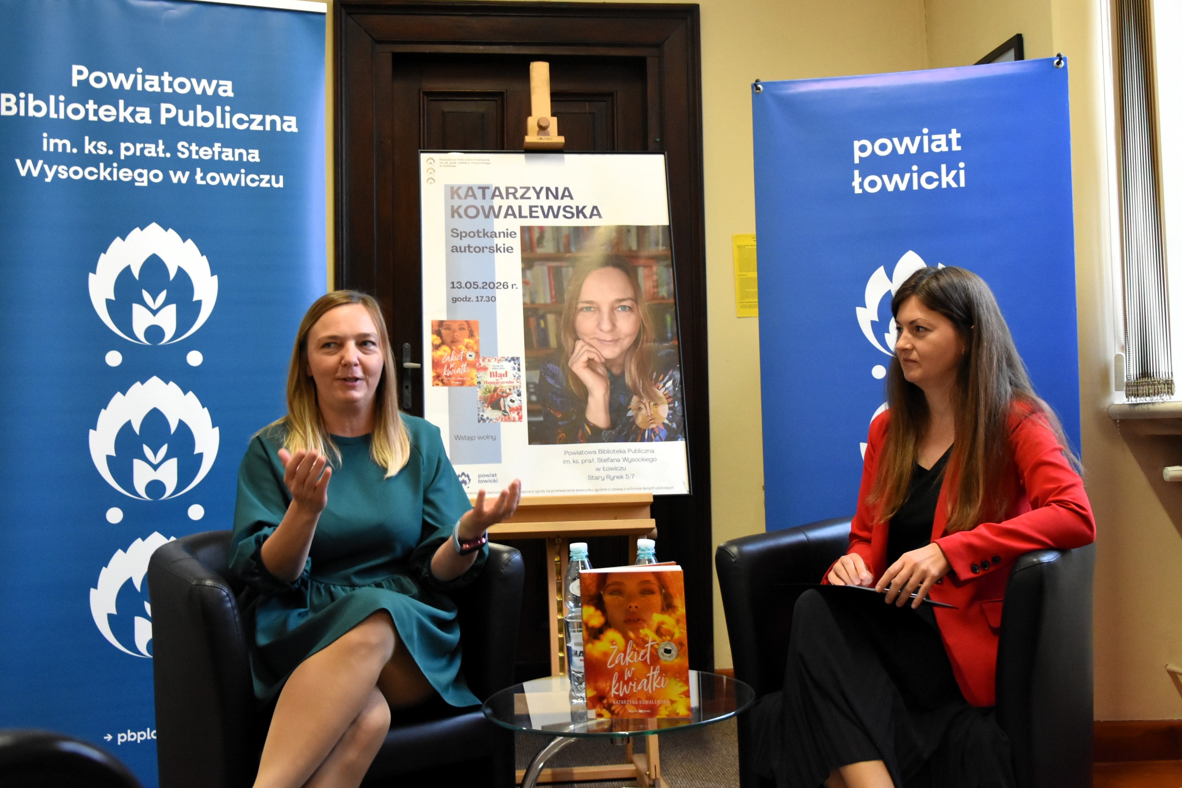 Dwie kobiety siedzą na fotelach w bibliotece i rozmawiają.